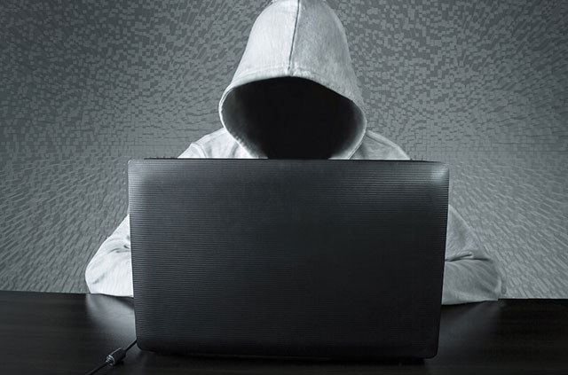 A person in a hoodie, wit their face obscured, using a laptop.