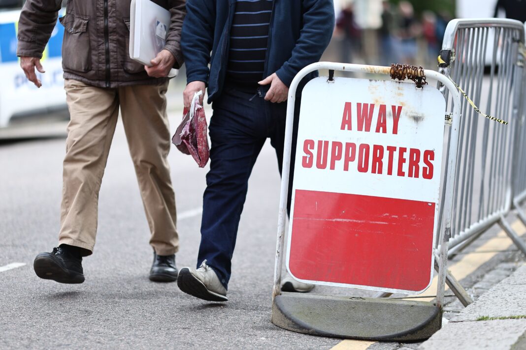 Football fans walk past an away supporters sign